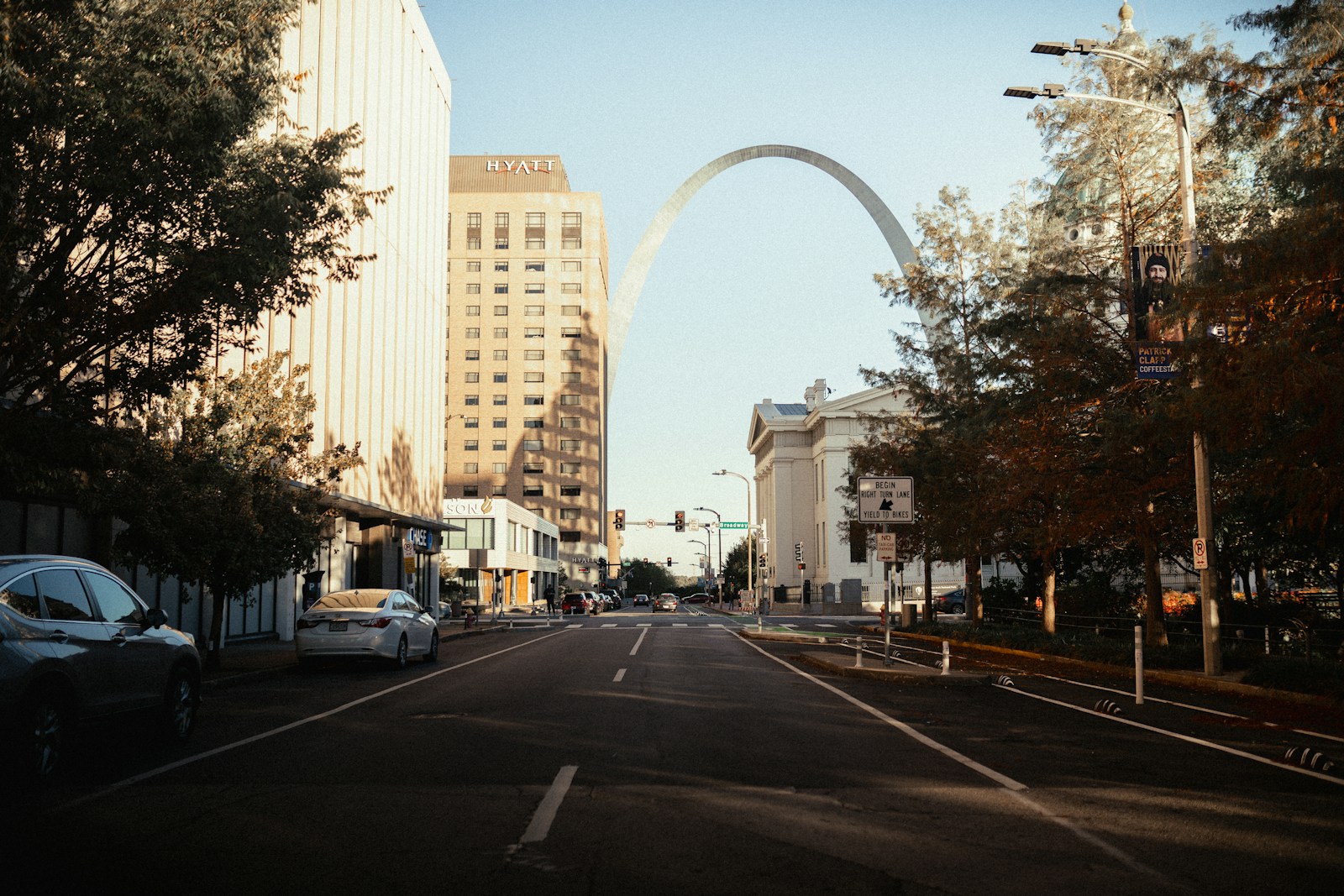 Brick buildings and trees line a downtown Saint Louis street, with the Gateway Arch in the distance.